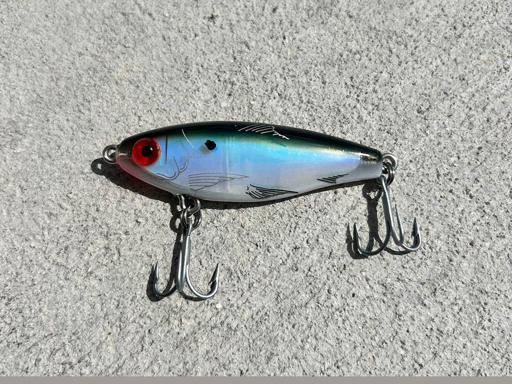 A closeuo of a blue-silver twitch-bait lure with two double-edged hooks on a concrete background