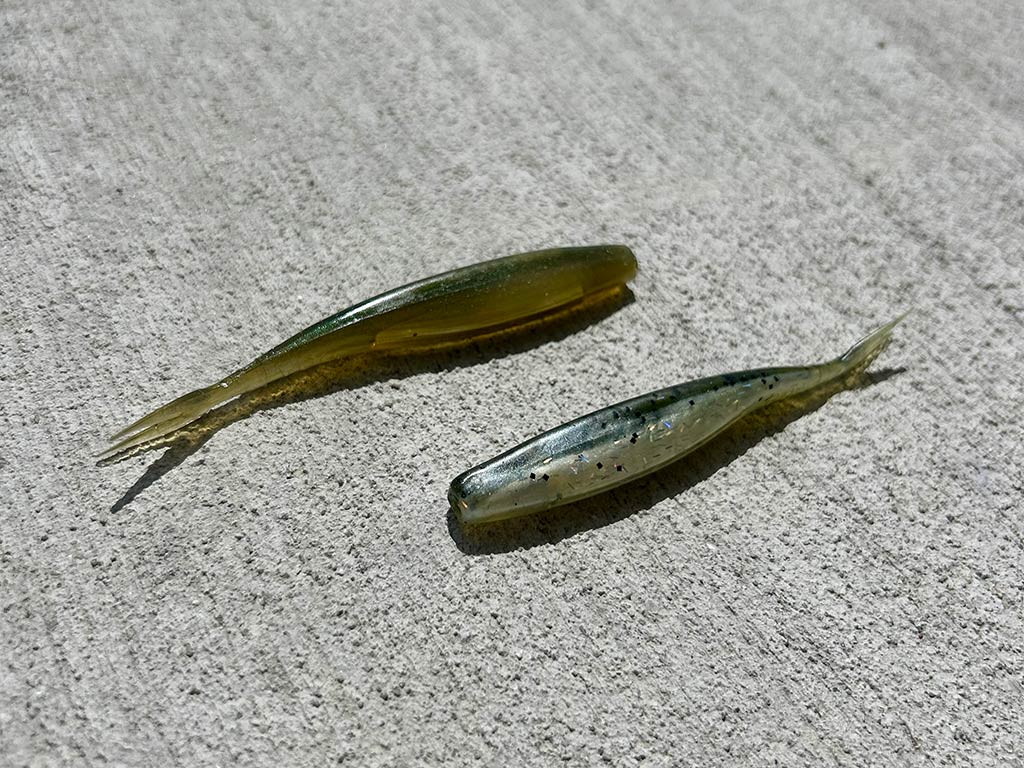 A closeup of two small fluke baits lying on a concrete background, ready to use for saltwater fishing