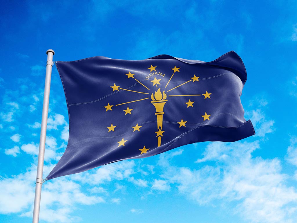 The state flag of Indiana flying in the wind from a flagpole against a clear blue sky