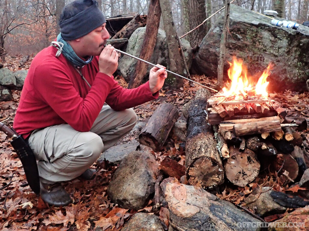 Photo of a man blowing into a fire to stoke the flames.