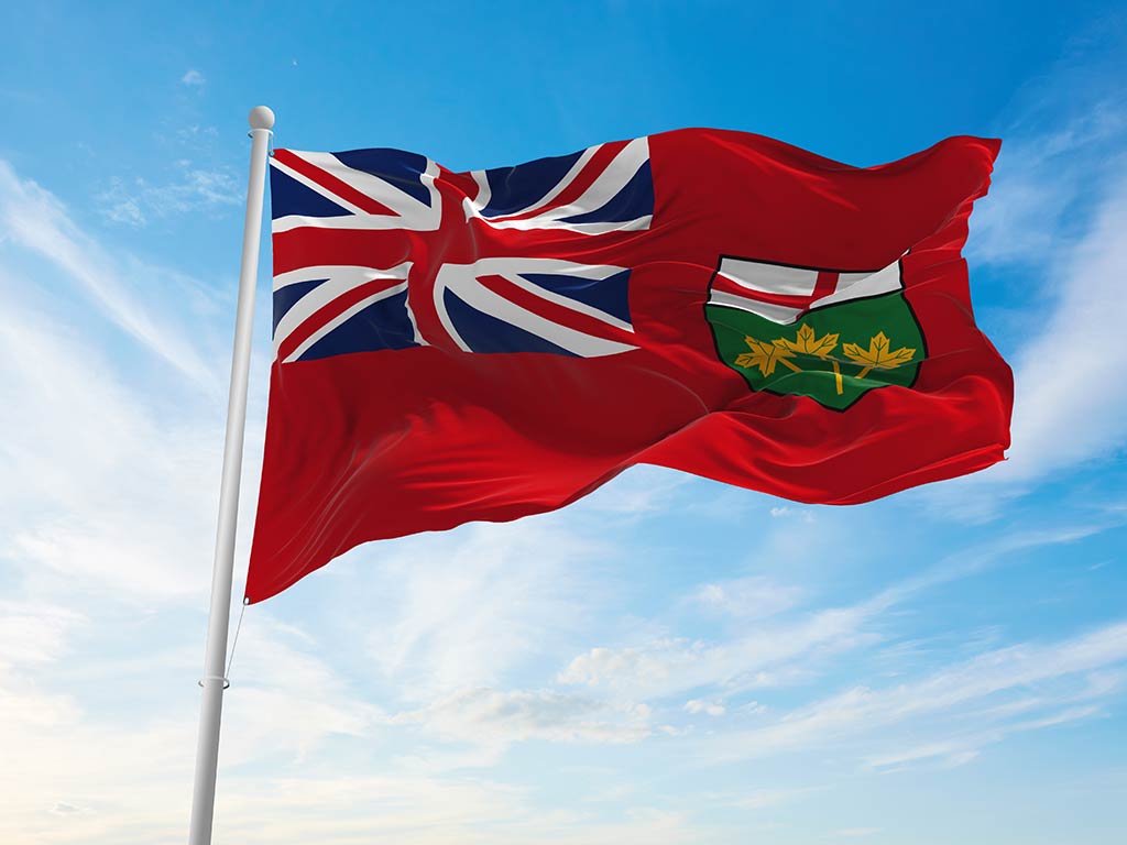 The flag of Ontario flying in the wind from a flagpole against a clear blue sky
