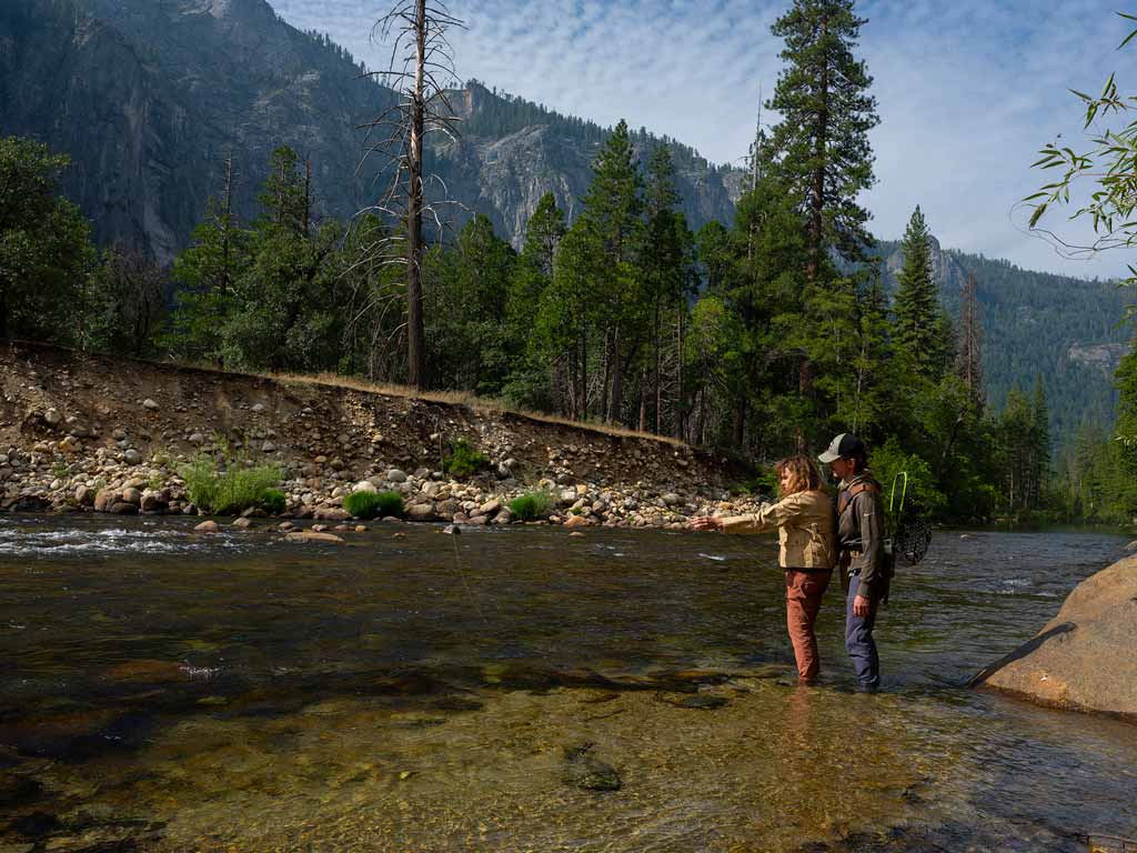 A pair of anglers fishing by a river's shore in Yosemite National Park, which is one of the best destinations to visit in spring.