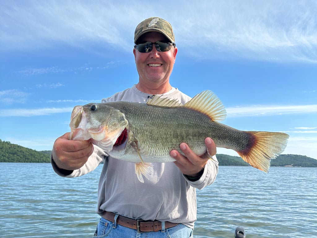An angler in sunglasses and a hat holding a sizeable Largemouth Bass he caught fishing on Lake Guntersville, one of the best spring fishing destinations in the US.