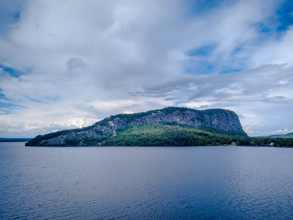 A scenic view of Mount Kineo taken from Moosehead Lake located in the heart of the Maine Highlands, with the calm lake waters and some clouds in the sky visible.