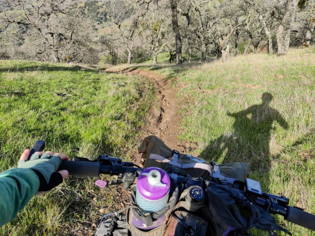 View over mountain bike handlebars down steep dirt trail