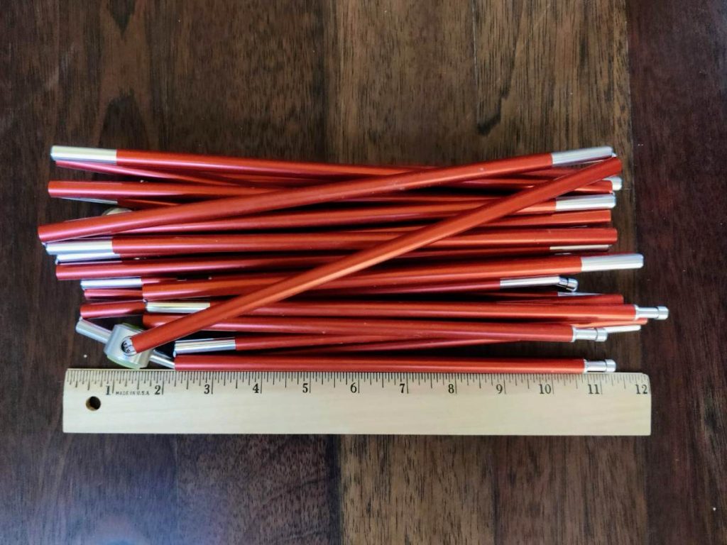 Folded bundle of red tent poles next to 12 inch ruler