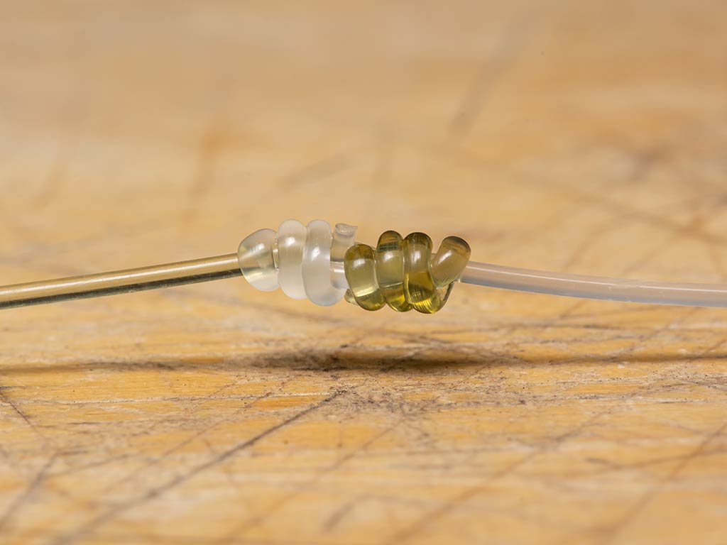 A closeup of two monofilament lines - one white and one gold -knotted together above a wooden table