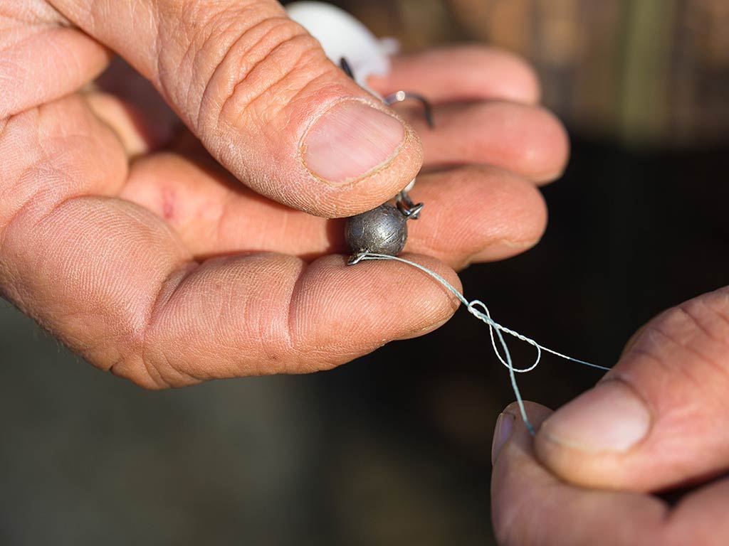 A closeup of a pari of hands holding a weight and displaying the knot tied to ensure it stays connected to the rest of the tackle
