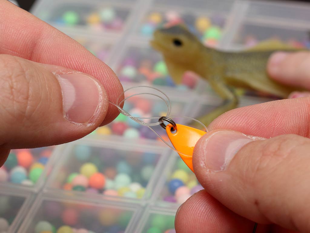 A closeup of a pair of hands holding a small fishing spoon and displaying the knot made to keep it on the line