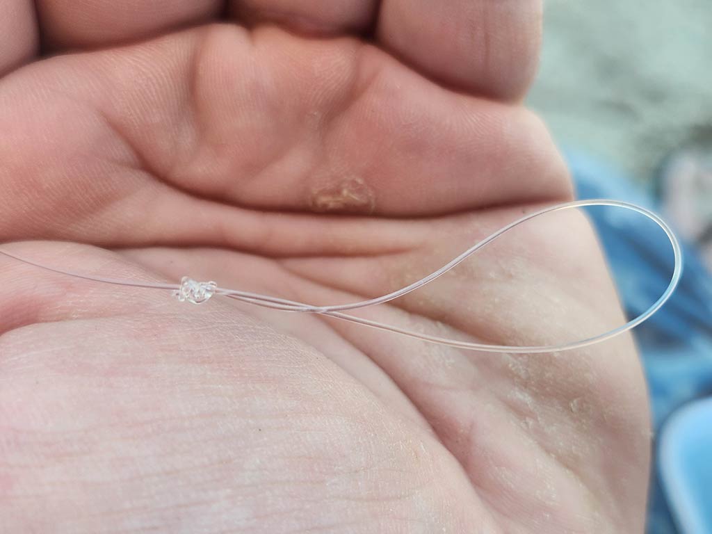 A closeup of a piece of fishing line tied into a loop using a surgeon's knot against the hand that's holding it