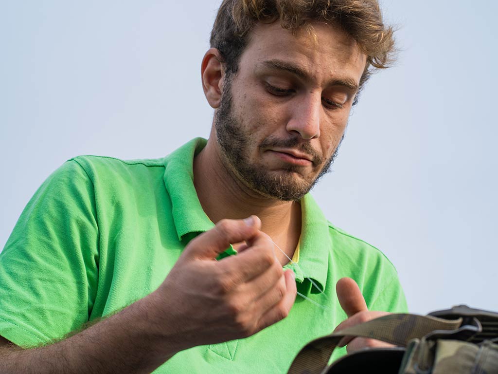 A man in a green shirt focuses as he ties a knot before going fishing