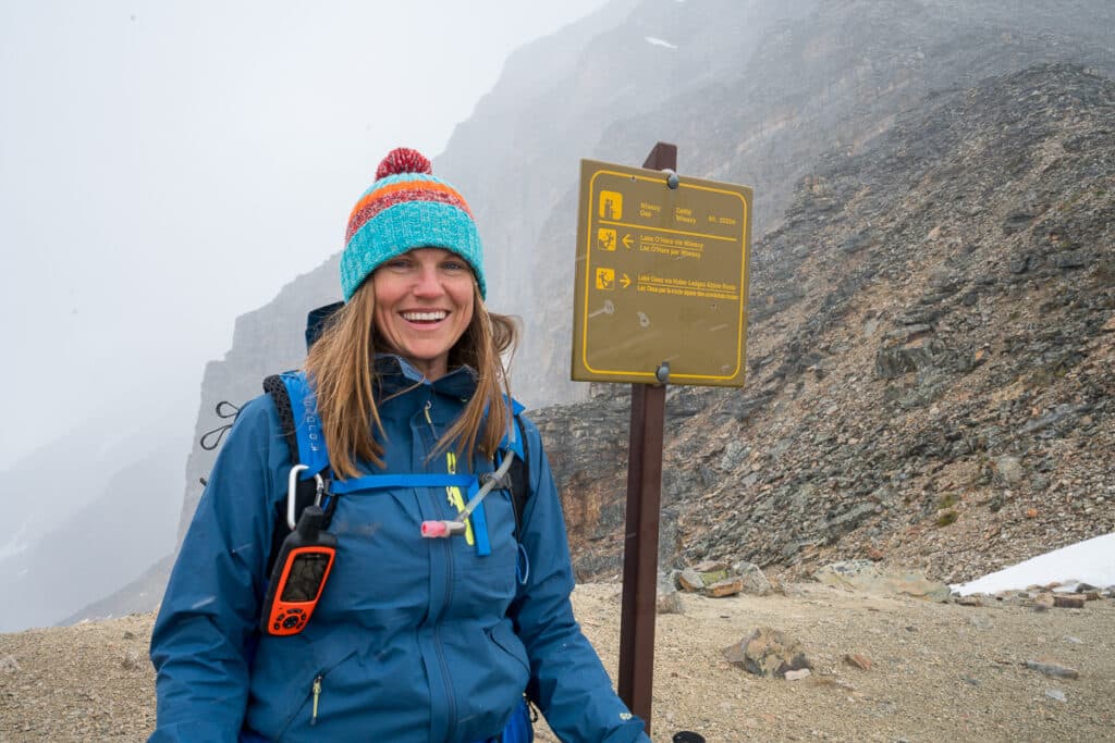Bearfoot Theory founder Kristen Bor hiking on a foggy rainy day at Lake O'Hara. She is standing next to a trail sign.