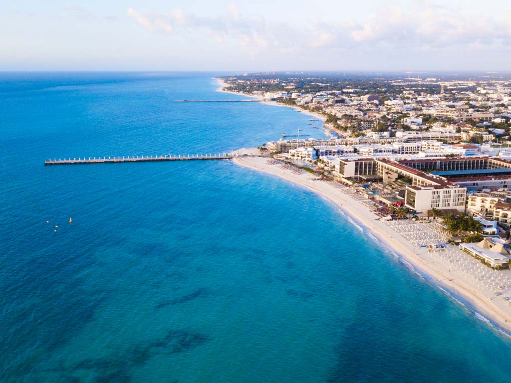 An aerial shot of Playa del Carmen in Mexico, with a fishing pier stretching from the city's coast into the blue ocean waters. 