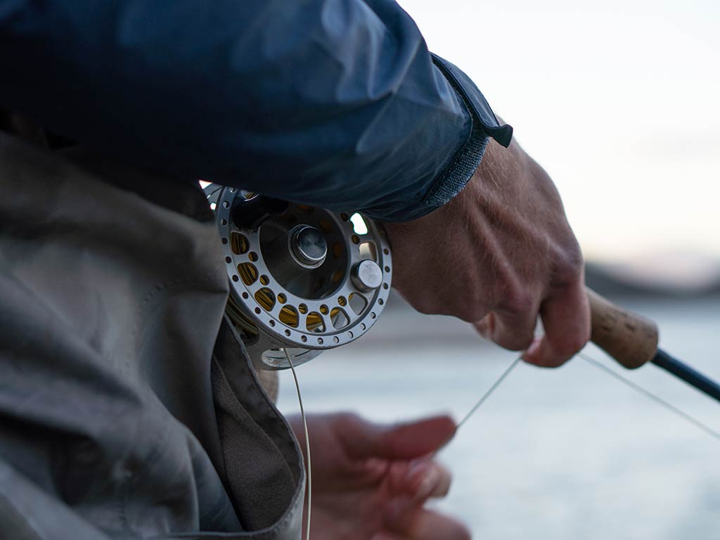 A closeup of a fly fishing reel in action as an angler holds their line out of focus