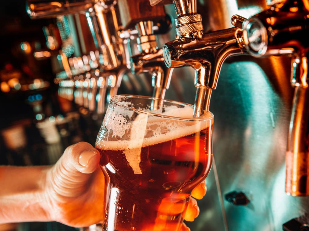 A photo featuring a hand holding a glass and filling it in with draft beer from the tap in a bar