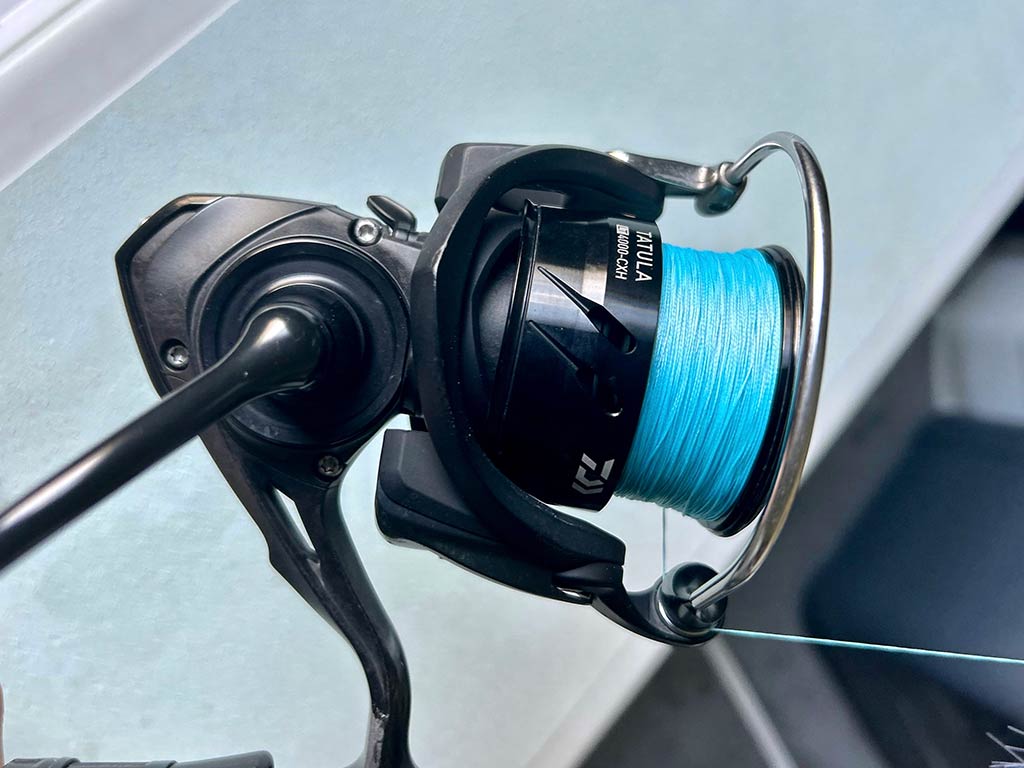 A closeup of a Daiwa Tatula 4000 reel with a blue line, ready for saltwater fishing