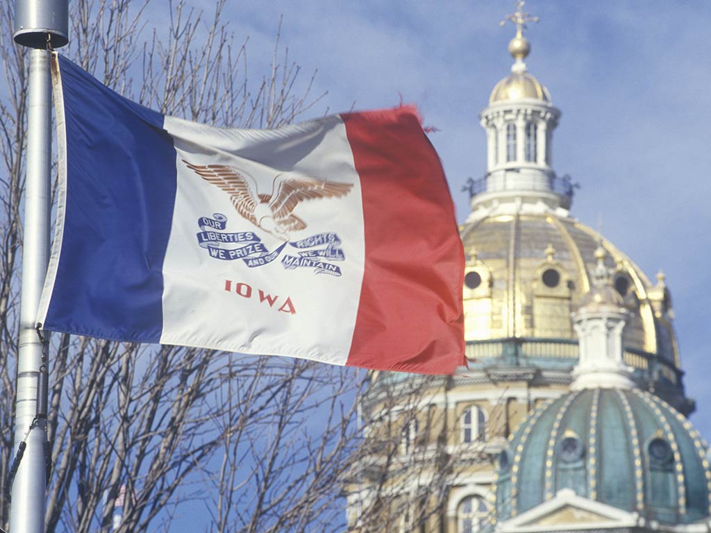 A view of the Iowa state capitol building behind a fluttering flag of the state on a hazy day