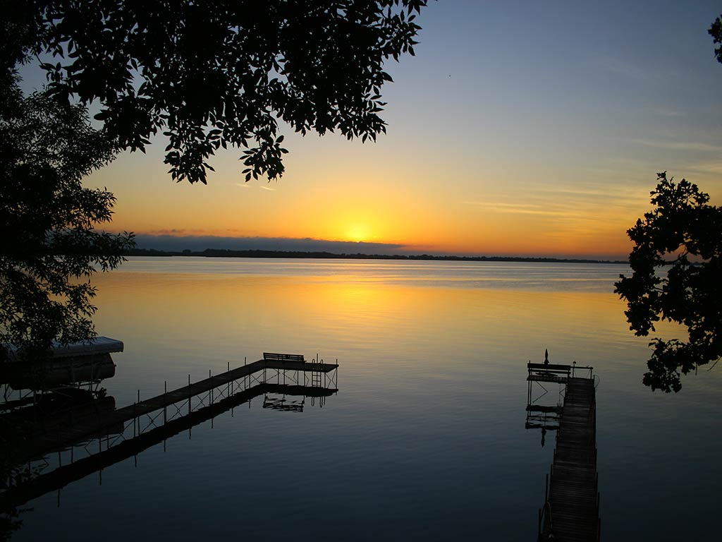 A ciew across a small dock towards the vast expanse of Spirit Lake in Iowa at sunset, with the sun setting in the distance