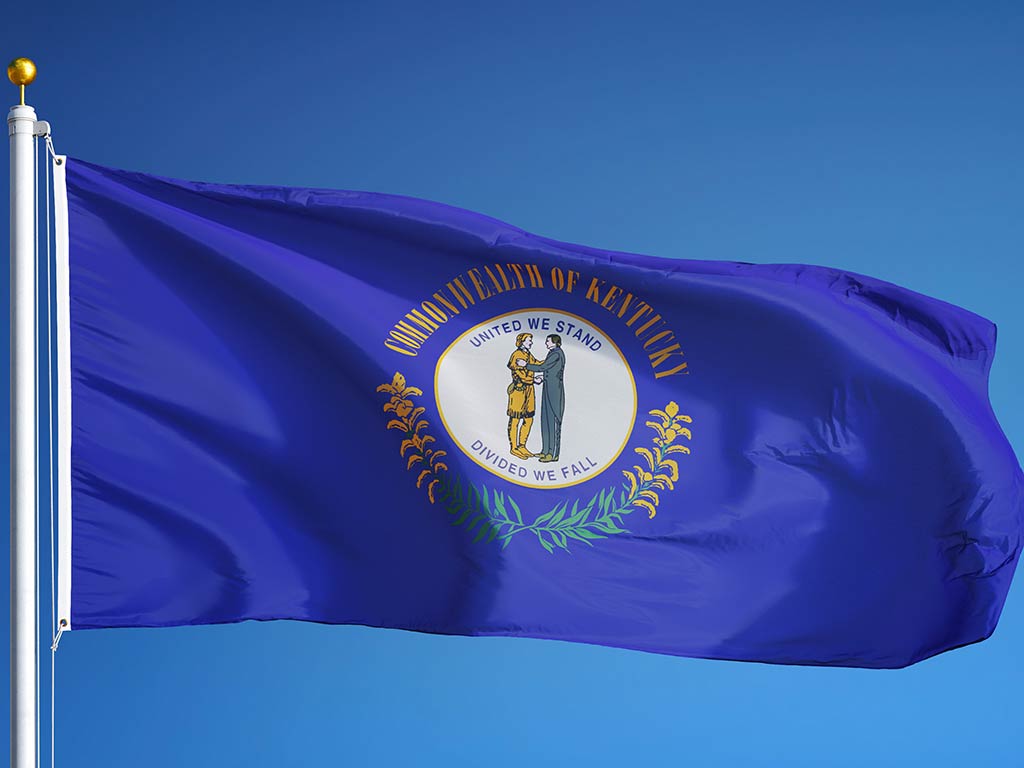 The state flag of Kentucky flying from a flagpole against a blue sky on a clear day