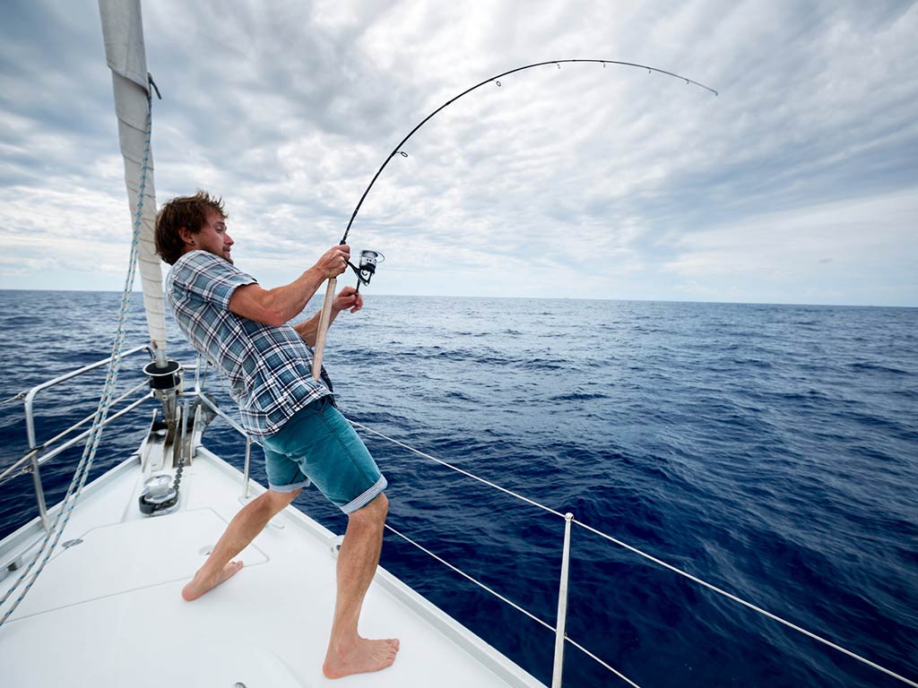 A man struggles with a fishing rod on an offshore sportfishing boat, as he tries to battle a fish that he's hooked