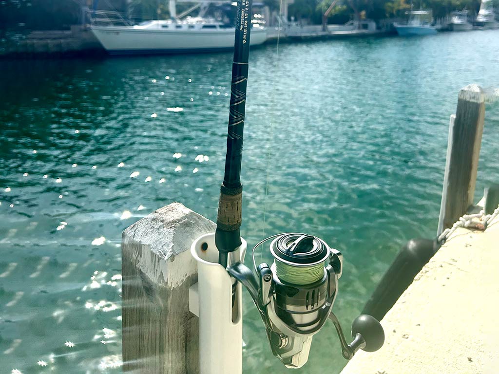 A closeup of a Star Rods Plasma fishing rod and reel set up on a dock in Florida with a boat visible across the water in the distance on a sunny day