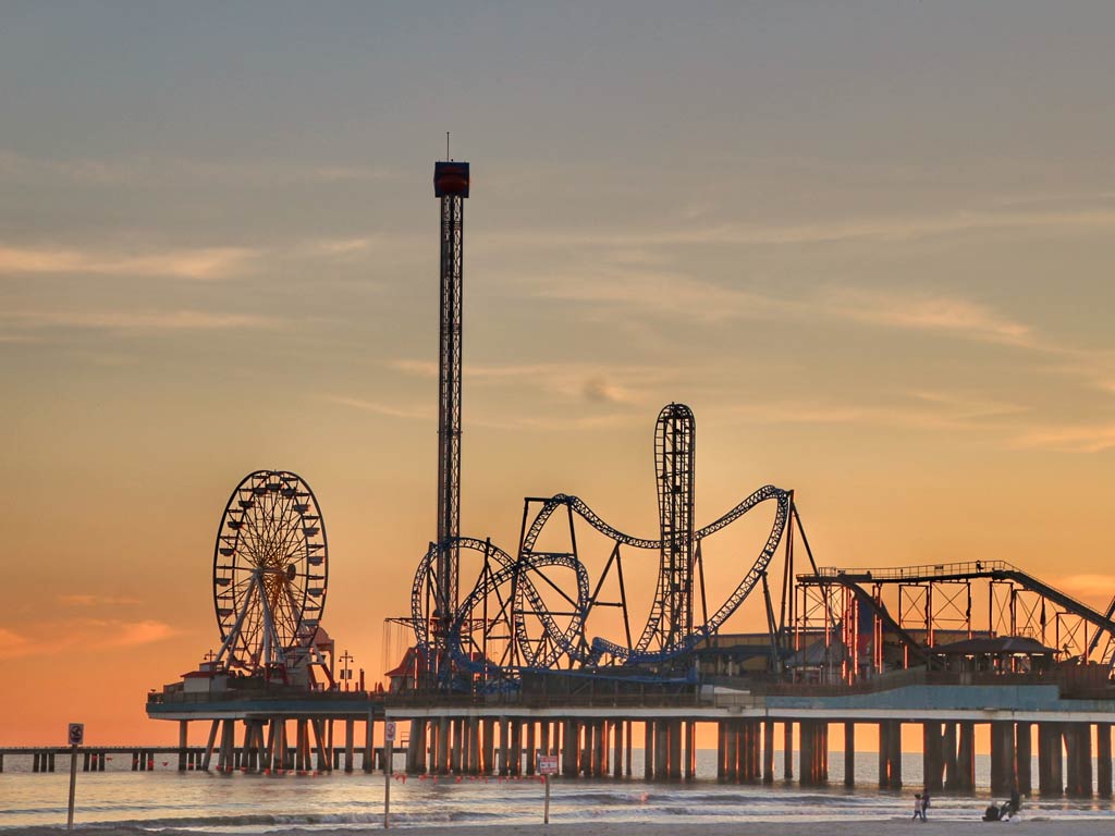 A photo featuring Galveston Island Historic Pleasure Pier and its roller coasters, panoramic rides, and carnival games during the sunset