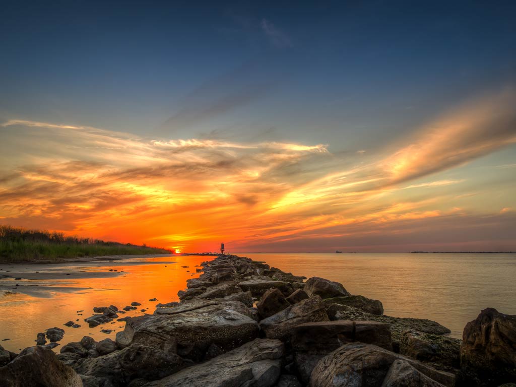 A photo featuring a sunset view over the jetties and bay in Galveston