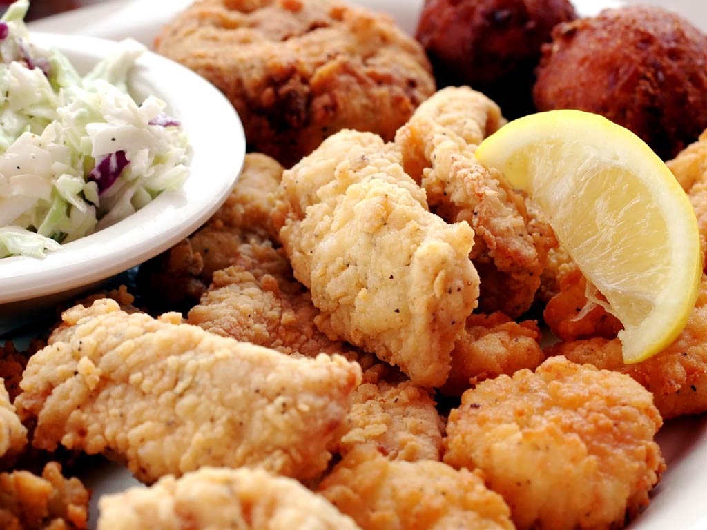 A photo featuring a seafood platter full of fried fish, hush puppies, and other seafood bites served on a plate with lemon and salad 