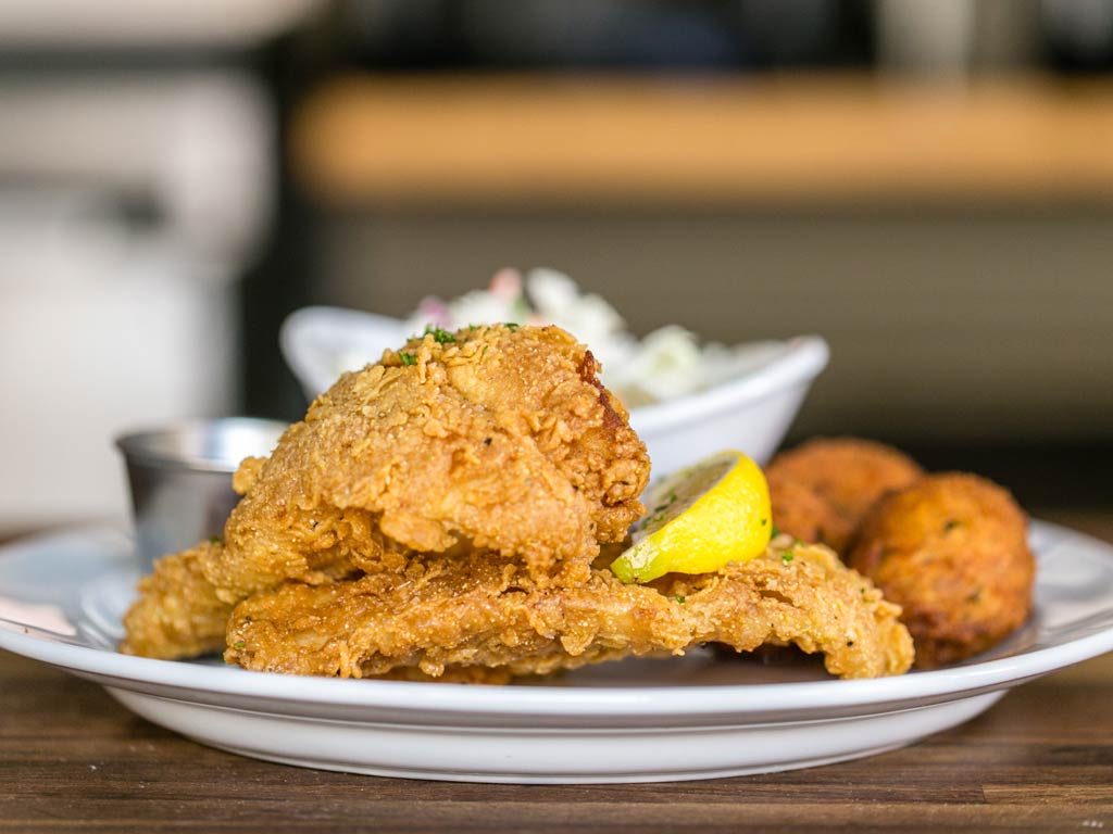 A photo featuring a typical Galveston catch-and-cook deep fried fish fillet and served on a plate with two hush puppies, lemon, sauce, and salad