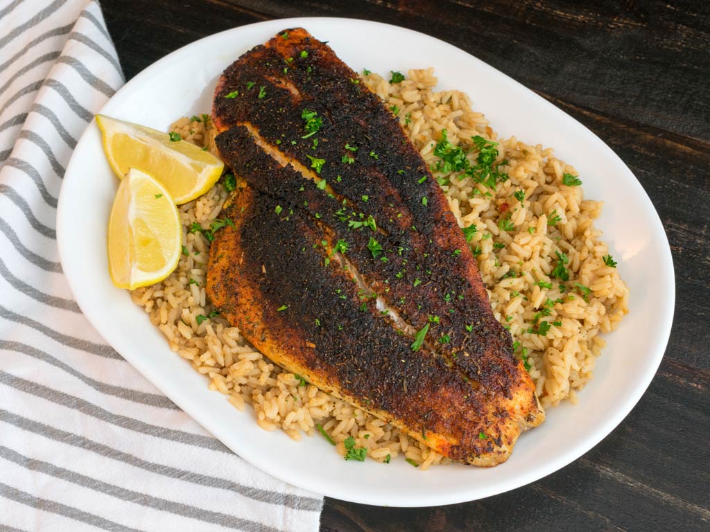 A photo featuring a Cajun-blackened Redfish served on a plate with lemon and dirty rice, delicious and finger-licking good, just the way your Galveston catch-and-cook meal should be