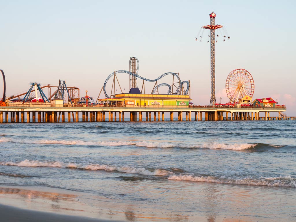 A photo featuring Galveston Island Historic Pleasure Pier and its roller coasters, panoramic rides, and carnival games at sunrise