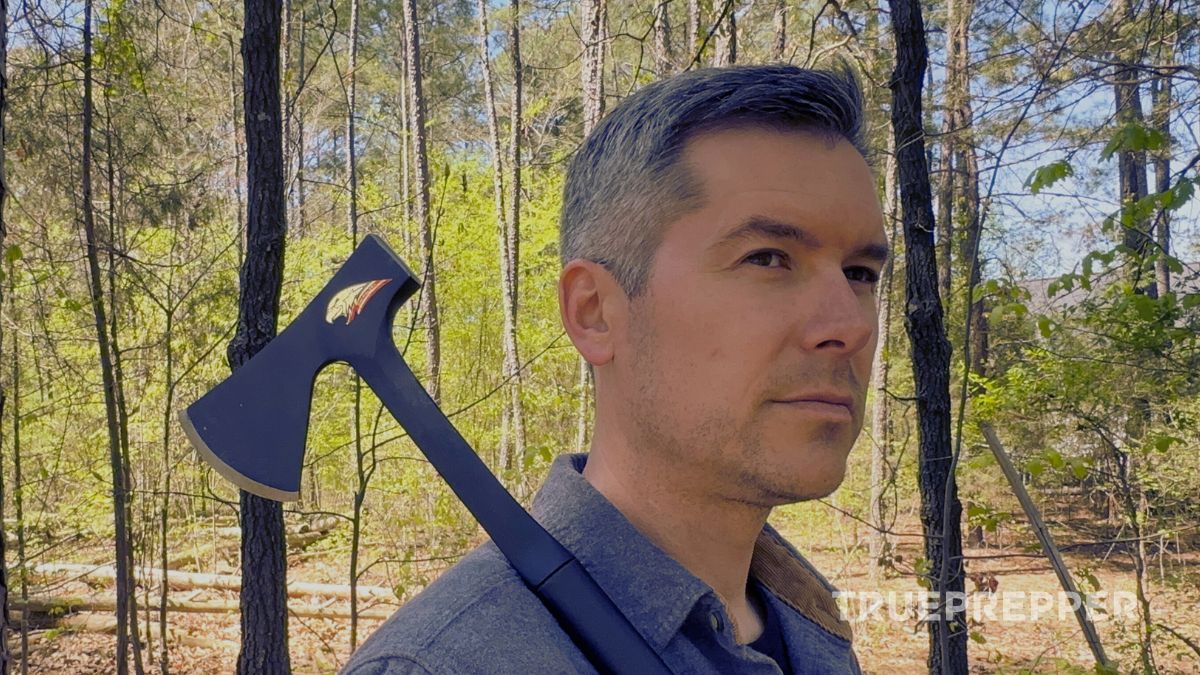 A man with a camp axe over his shoulder in the woods.