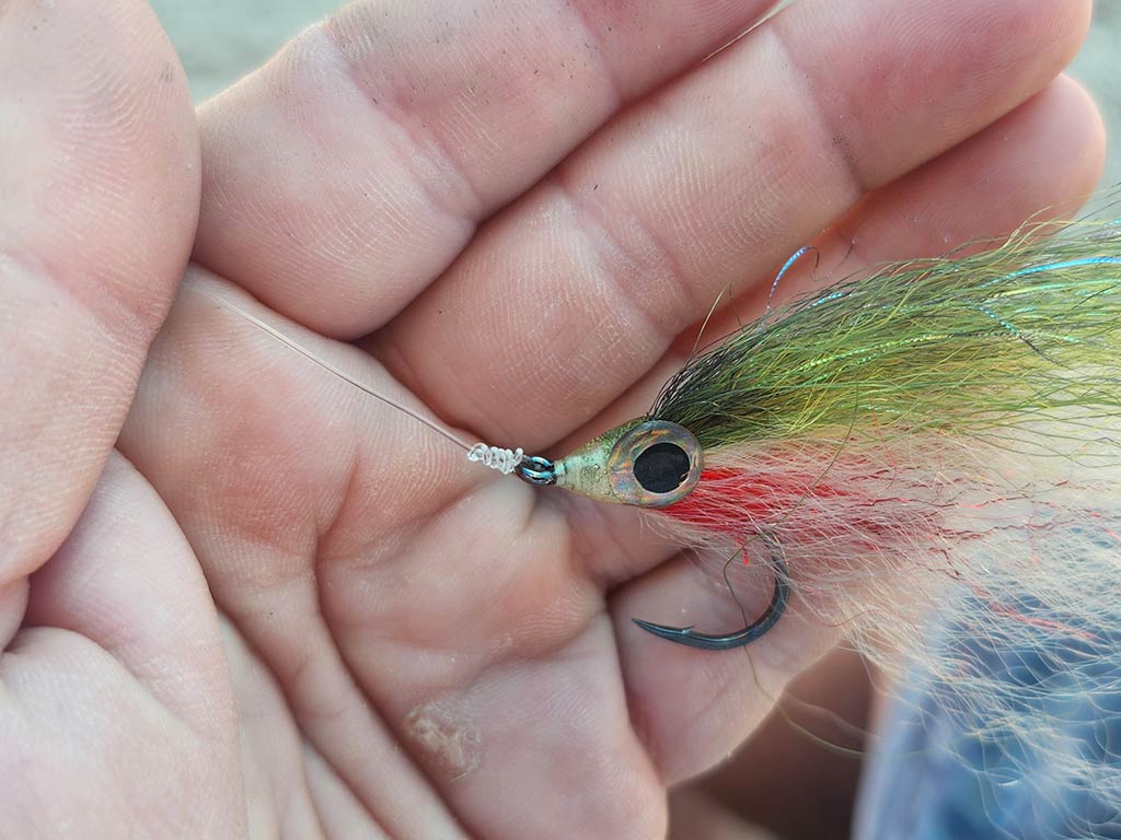 A closeup of a colorful lure tied to the end of a fishing line by an improved clinch knot, visible against the hand that's holding it