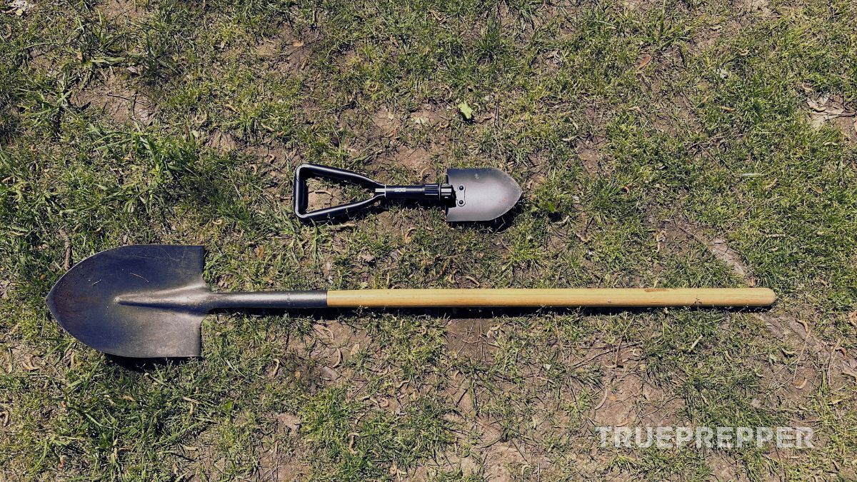 Entrenching tool laying on the ground above a standard spade, showing a size difference.