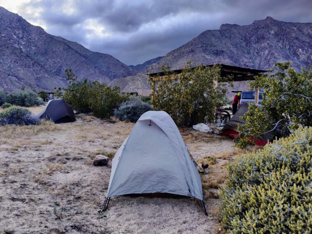 Solo tent in desert scrub at the Borrego Springs campground, with mountains and storm clouds in background