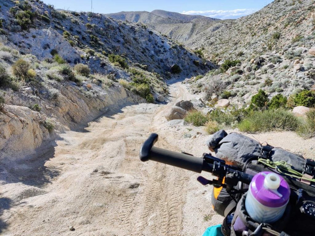 Rocky and sandy desert jeep road with mountain bike handlebar in foreground