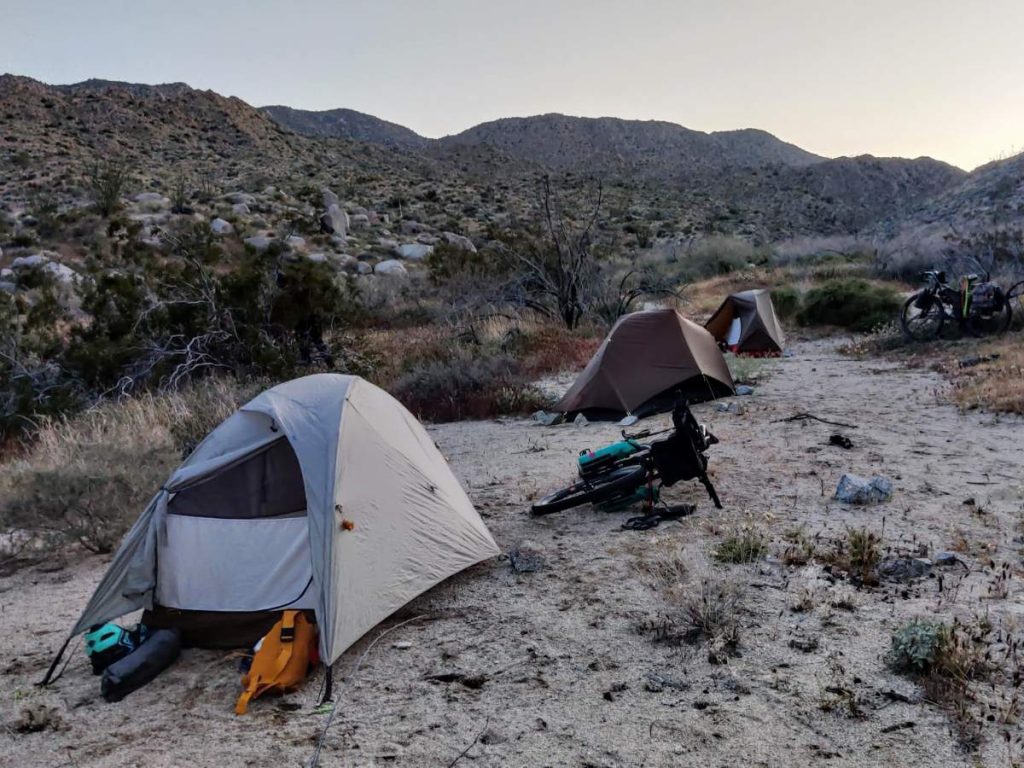 Three bikepacking tents at dusk in a sandy desert campsite