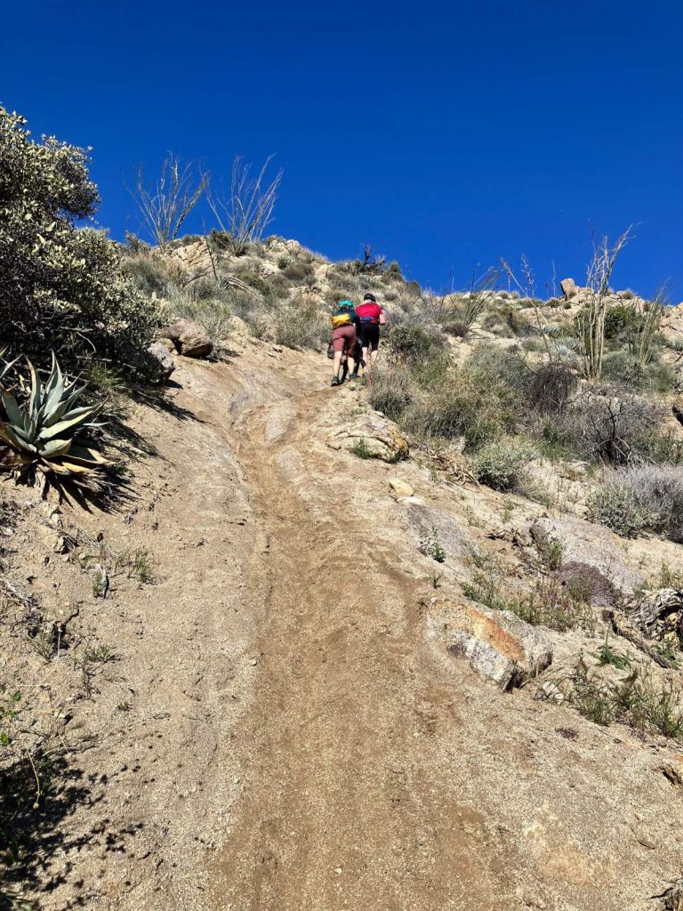 Two women push a loaded bikepacking bike up a steep desert trail