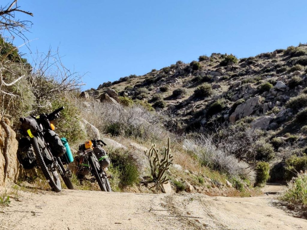 Two bikes lean against dirt embankment beside a desert backroad