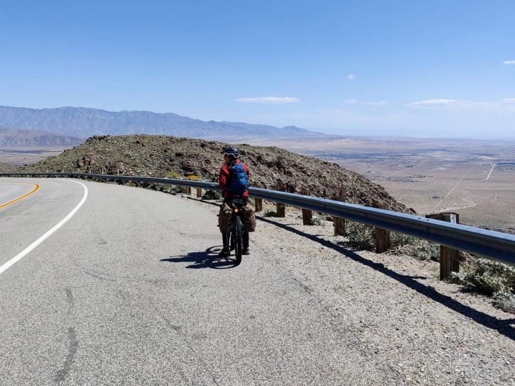 Cyclist pulled over in wide shoulder with views of brown desert floor ahead