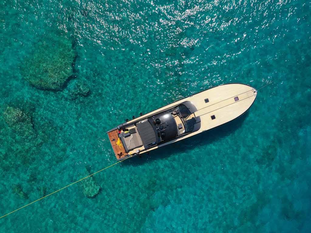 An aerial view of a boat and a harness dragging a drift sock behind in crystal clear waters on a sunny day
