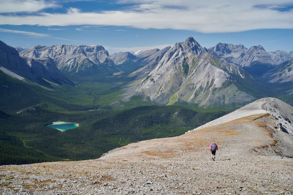 Hiker on Tent Ridge trail in Kananaskis, Alberta overlooking mountain range and alpine lake