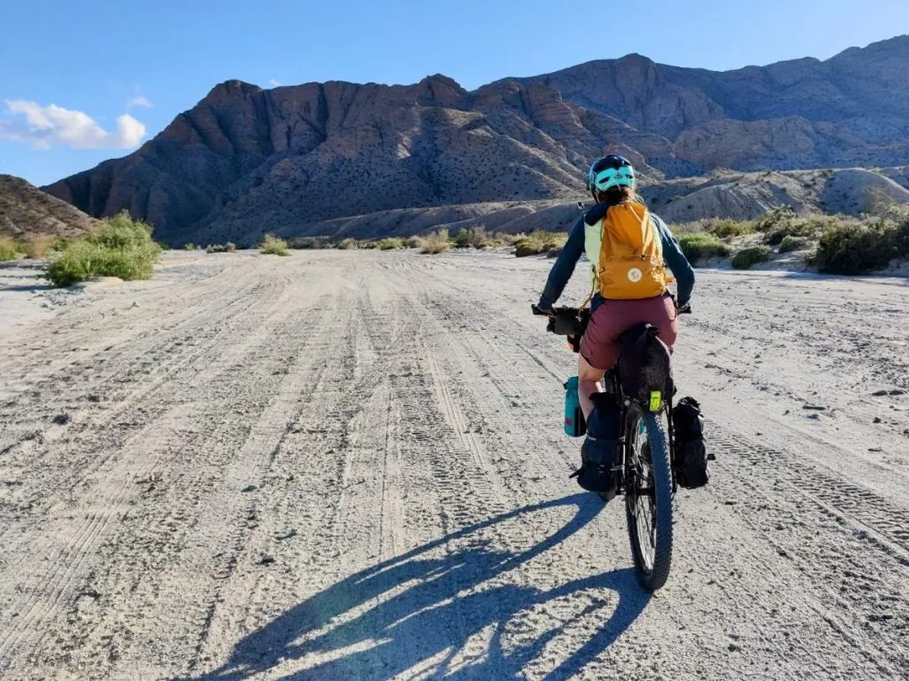 Bikepacker rides up desert wash with yellow S/F Expandable Hip Pack in backpack mode