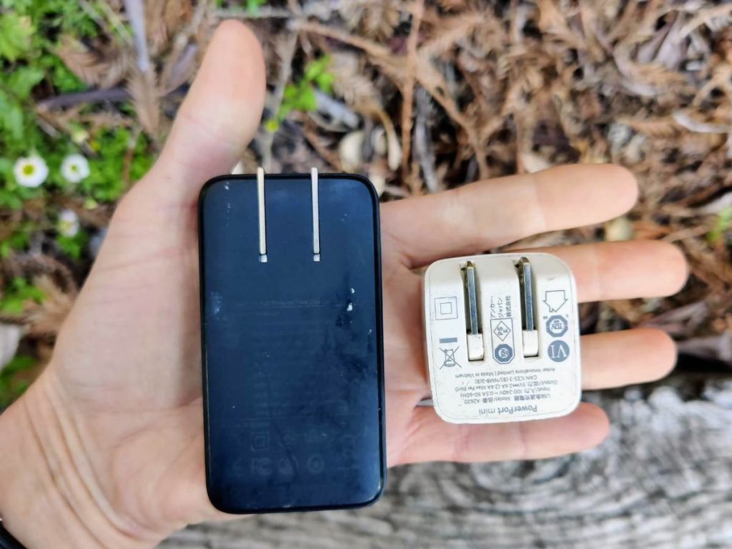 Hand holding two small wall chargers with folding prongs, ideal for bikepacking
