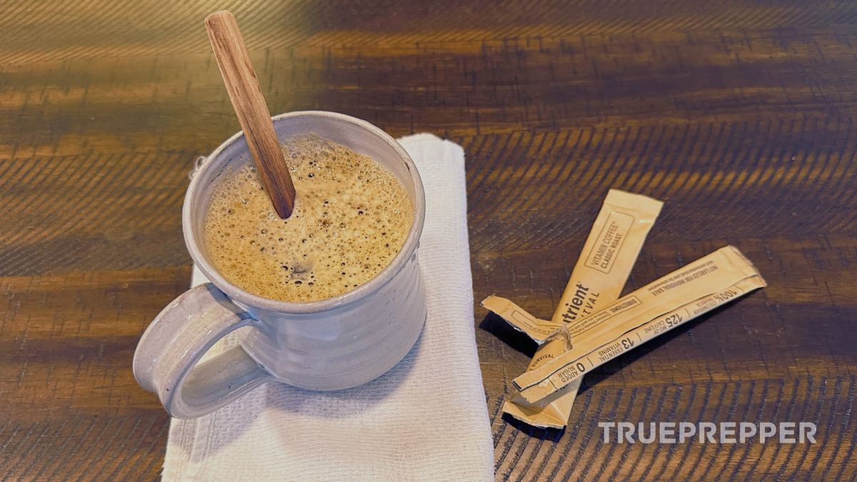 A mug of Nutrient Survival instant coffee with wooden stirrer and empty packet on a table.
