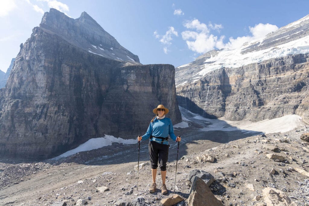 Female hiker standing on trail near Lake Louise, BC for photo with barren, rocky, and snow-covered peaks as backdrop