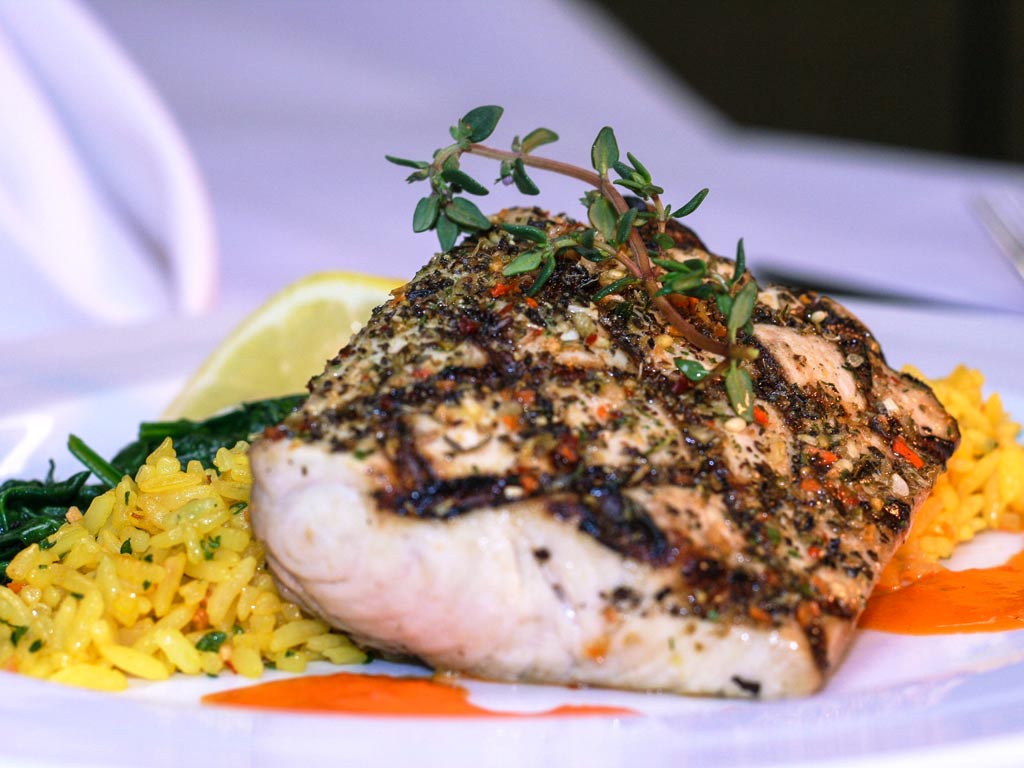 A closeup photo of a grilled Mahi Mahi filet on a bed of rice, topped with spices and garnish. The image serves as an illustration of the kind of meal you can expect when you take your catch to be cooked.