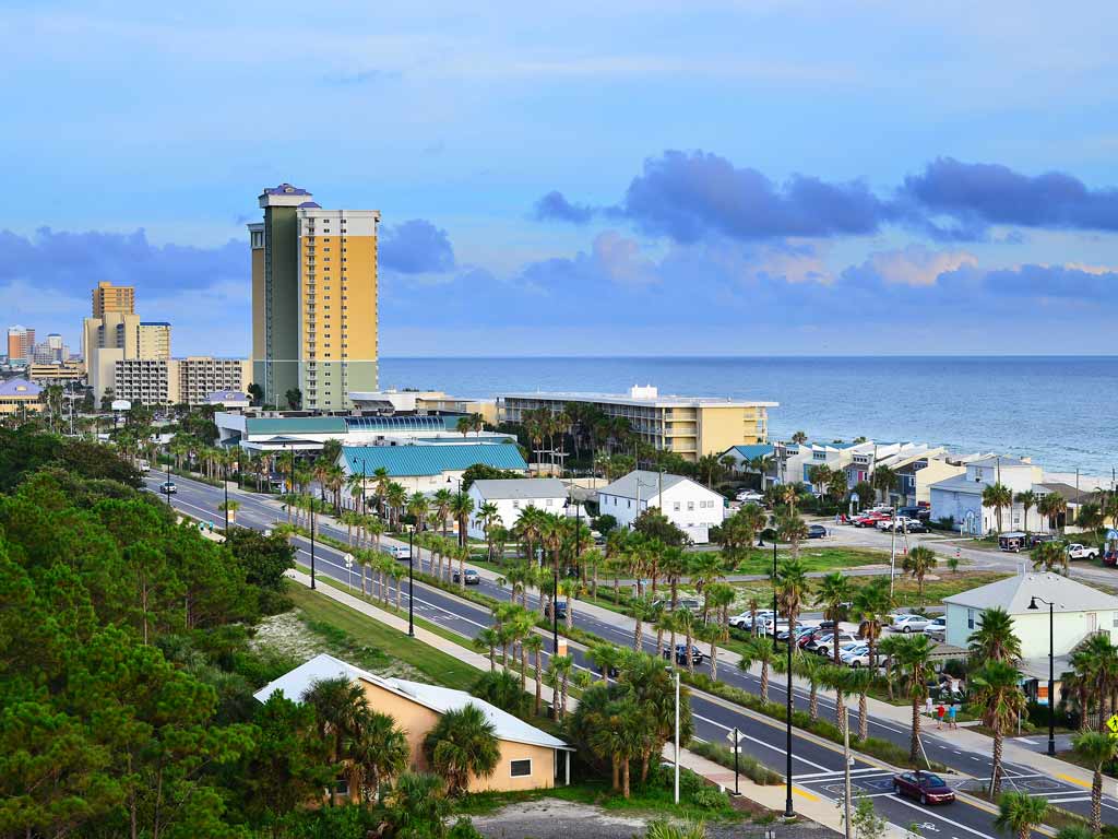 A cityscape photo of Panama City Beach, Florida, looking along Front Beach Road at dusk, with the road intersecting the photo diagonally and city buildings visible behind it.