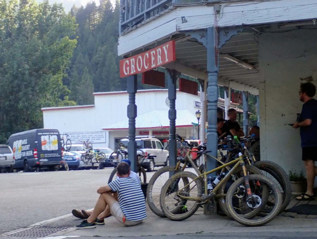 Mountain bikers sit beside their bikes in front of a small town grocery store