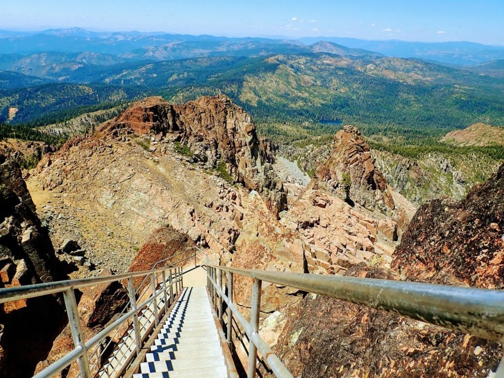 Looking down steep metal stairs from lookout tower with view of mountain range in the Lost Sierra